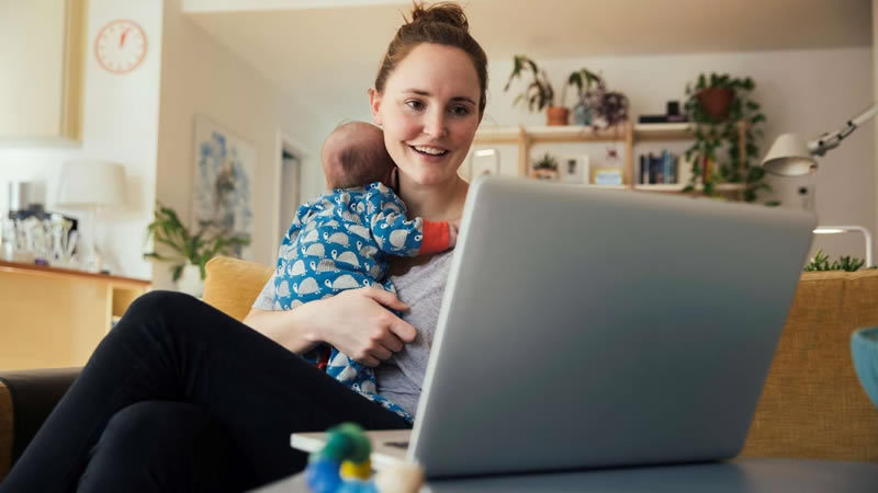 一位抱着婴儿的妇女在她的笔记本电脑前